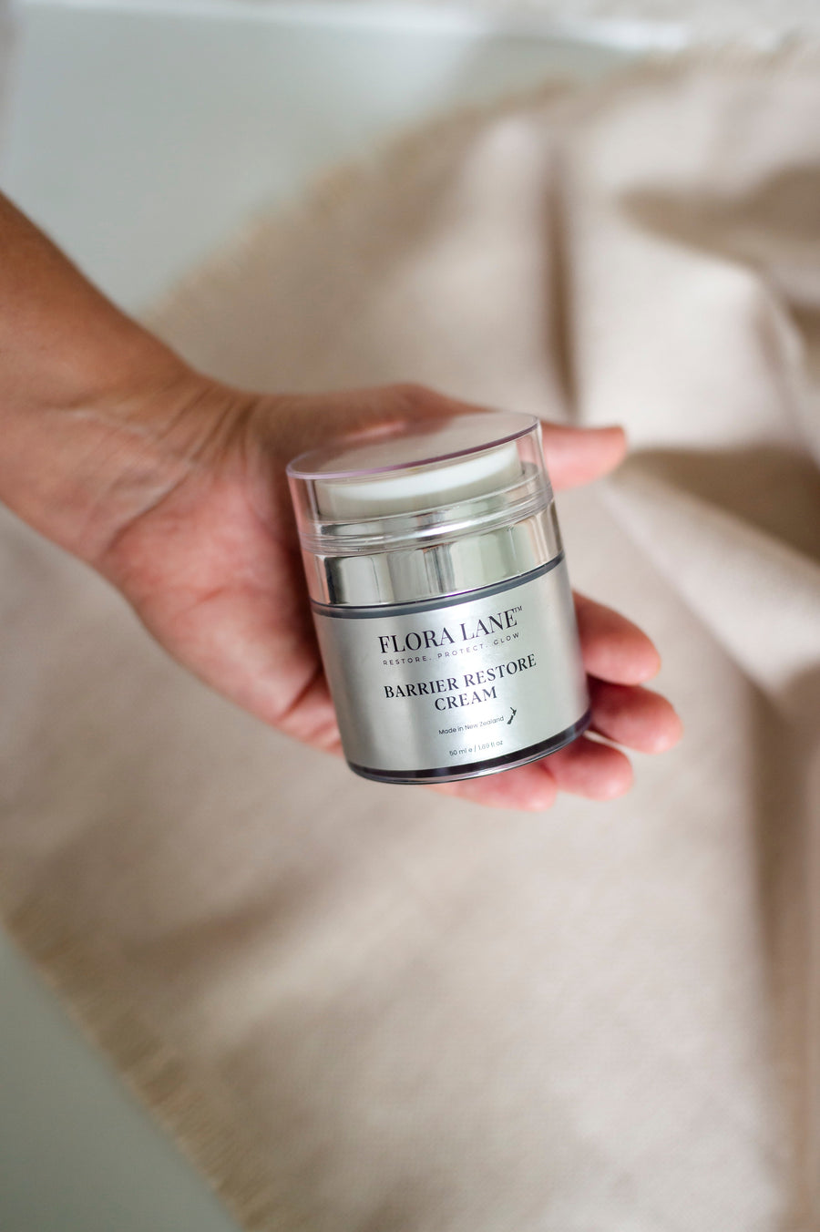 Hand holding Flora Lane Barrier Restore Cream on cream linen — best moisturiser for menopausal skin NZ